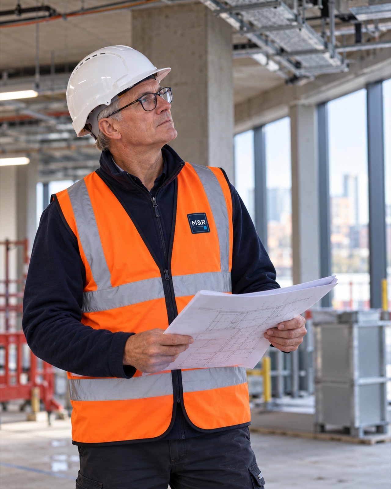 Tom Marlow, managing director, in a hard hat and hi-vis vest, reading a drawing on an office floor under construction.